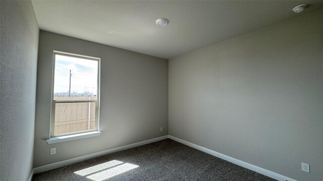 spare room with baseboards and dark colored carpet