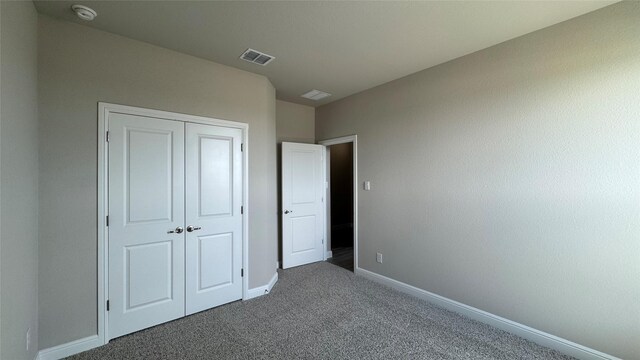 unfurnished bedroom with dark colored carpet, visible vents, baseboards, and a closet