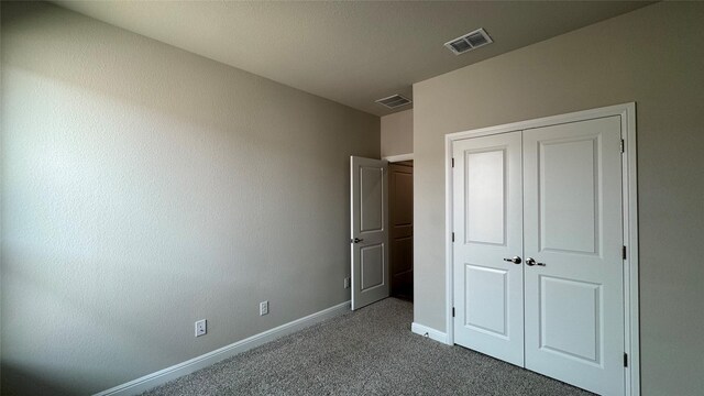 unfurnished bedroom with a closet, visible vents, baseboards, and dark colored carpet