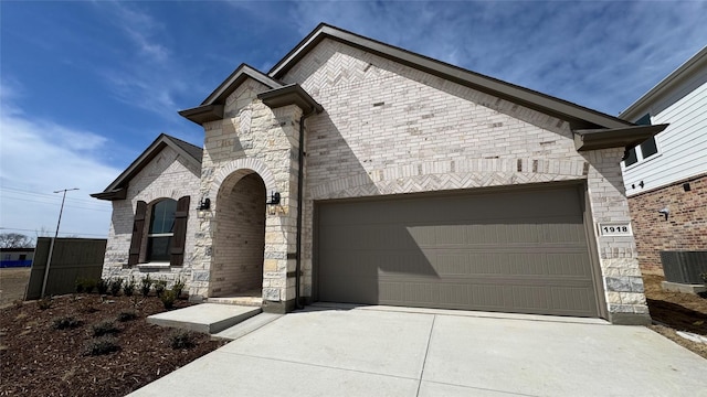french provincial home with concrete driveway, a garage, stone siding, and central AC
