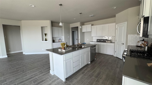 kitchen with dark countertops, tasteful backsplash, a sink, appliances with stainless steel finishes, and dark wood-style flooring