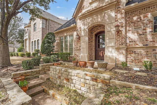 property entrance featuring brick siding and roof with shingles