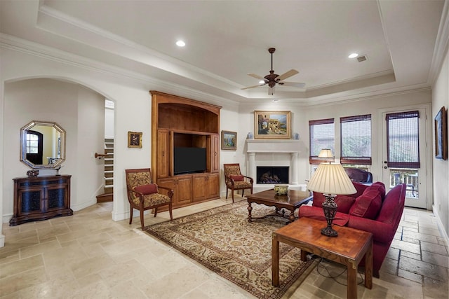 living room featuring stone tile floors, ceiling fan, a tray ceiling, and stairs