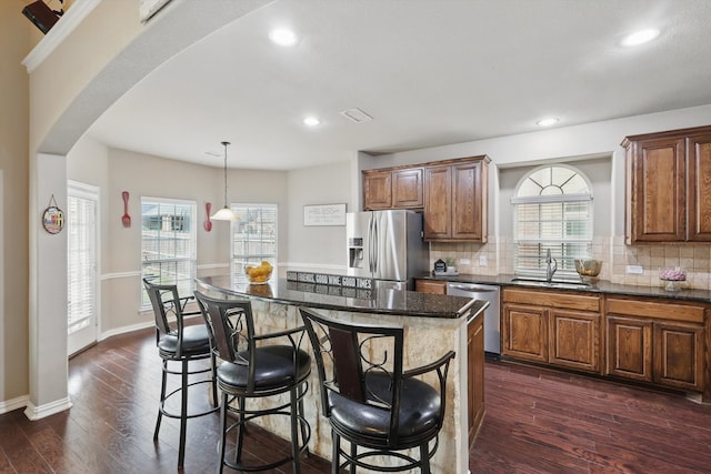 9645 Salvia Dr, Fort Worth, TX 76177 - kitchen with appliances with stainless steel finishes, arched walkways, dark wood-type flooring, a kitchen breakfast bar, and brown cabinets