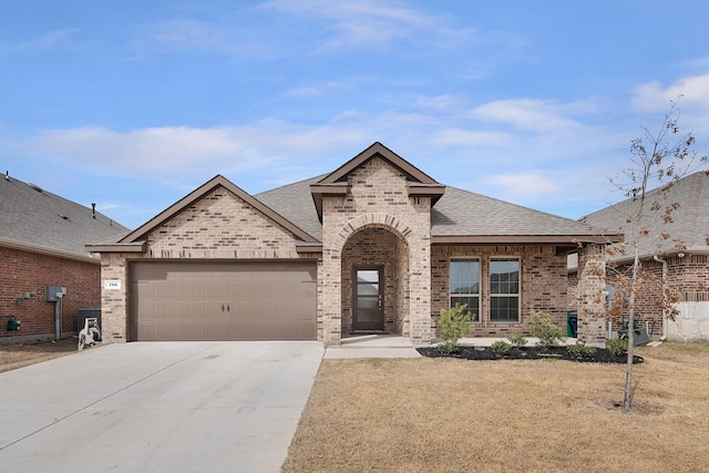 french country home featuring brick siding, an attached garage, driveway, and a shingled roof