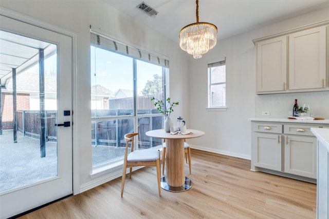 dining area with a notable chandelier, light wood-style flooring, baseboards, and visible vents