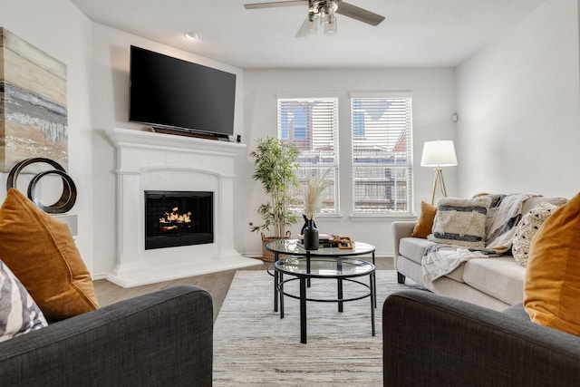 living area featuring baseboards, a warm lit fireplace, wood finished floors, and a ceiling fan