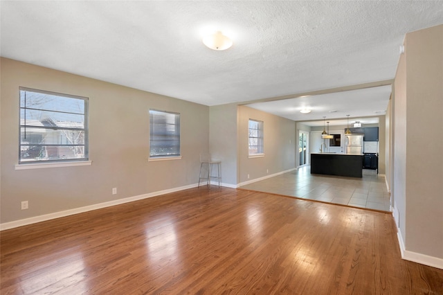4021 Kenley St, Fort Worth, TX 76107 - unfurnished living room with light wood-style flooring, baseboards, and a textured ceiling