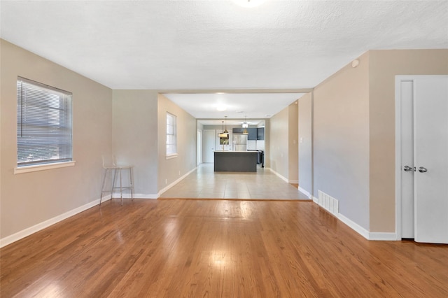 4021 Kenley St, Fort Worth, TX 76107 - unfurnished living room with light wood finished floors, visible vents, a textured ceiling, and baseboards