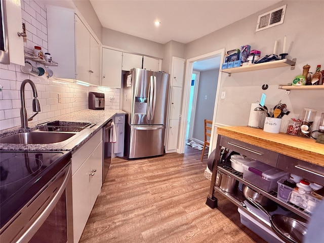 kitchen featuring stainless steel appliances, a sink, white cabinets, light wood-style floors, and backsplash
