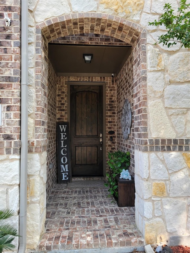 view of exterior entry featuring brick siding and stone siding