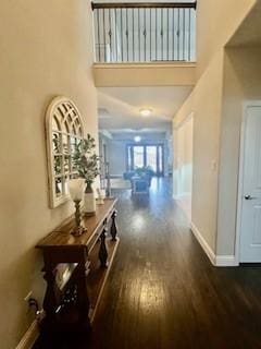 hallway featuring wood finished floors, a high ceiling, and baseboards