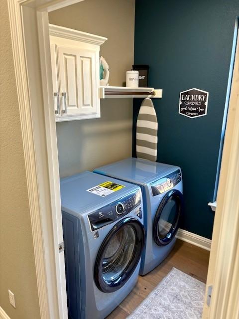 laundry area with washer and dryer, cabinet space, wood finished floors, and baseboards
