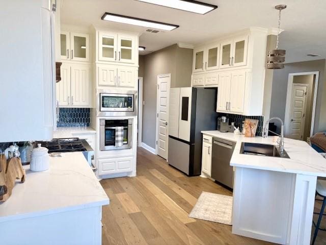 kitchen with appliances with stainless steel finishes, a sink, a peninsula, and white cabinets