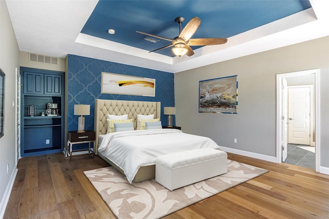 bedroom with baseboards, wood finished floors, a tray ceiling, and an accent wall