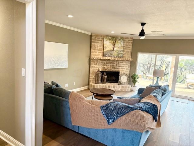 living area featuring ornamental molding, wood finished floors, a ceiling fan, baseboards, and a stone fireplace