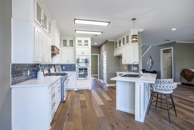 kitchen featuring stainless steel appliances, a breakfast bar area, wood finished floors, a peninsula, and a sink
