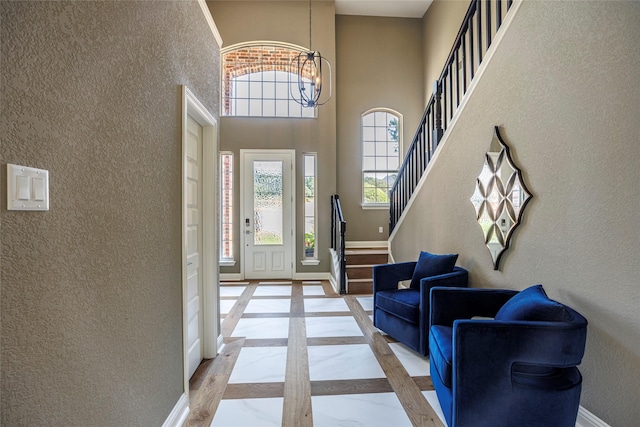 entrance foyer with baseboards, inlaid floor details, a chandelier, a towering ceiling, and a textured wall