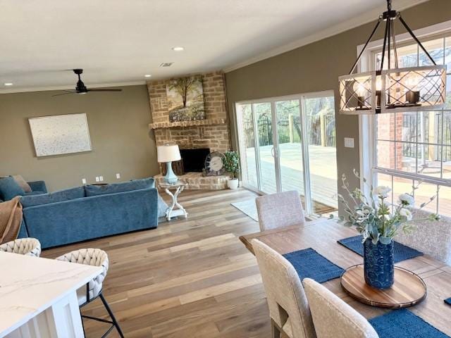 dining area with crown molding, ceiling fan, a fireplace, light wood-style flooring, and recessed lighting