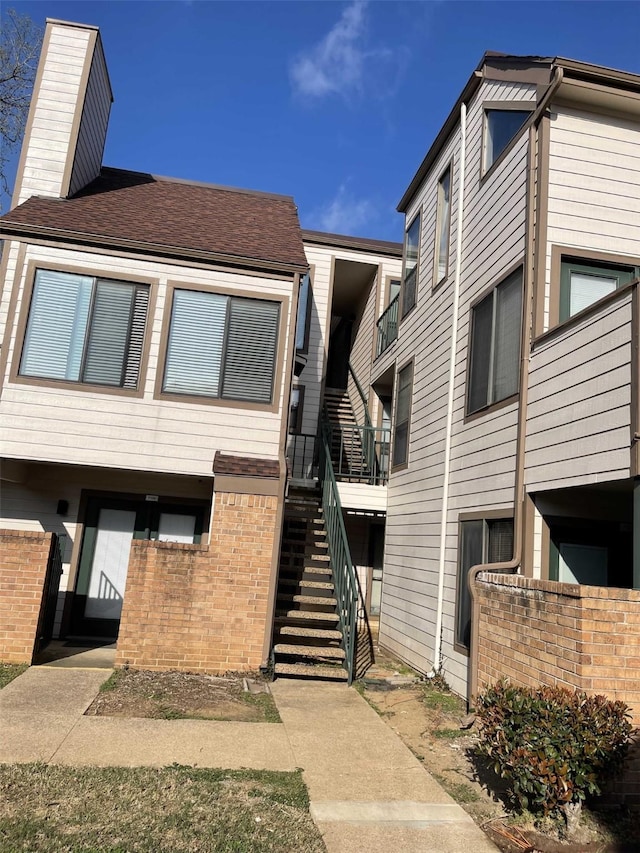 view of front facade featuring stairs, brick siding, and a chimney