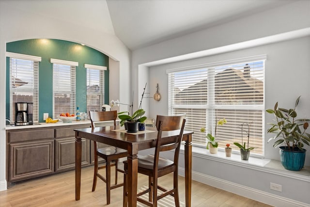 dining space with baseboards, light wood-style flooring, and vaulted ceiling