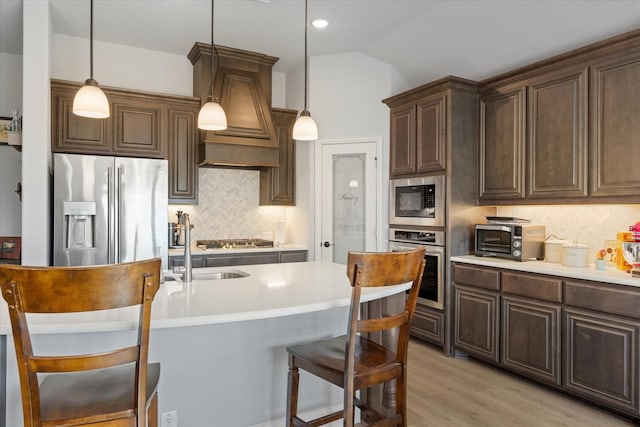 kitchen featuring a kitchen breakfast bar, stainless steel appliances, light wood-style floors, a toaster, and lofted ceiling