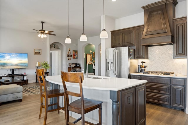 kitchen with custom range hood, a sink, arched walkways, stainless steel fridge with ice dispenser, and light countertops