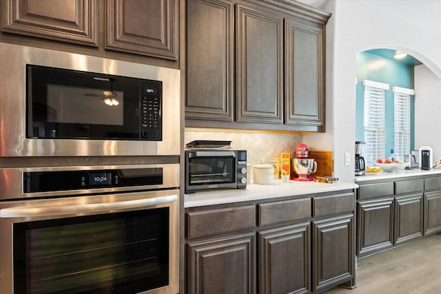 kitchen featuring light countertops, light wood-style floors, black microwave, stainless steel oven, and backsplash