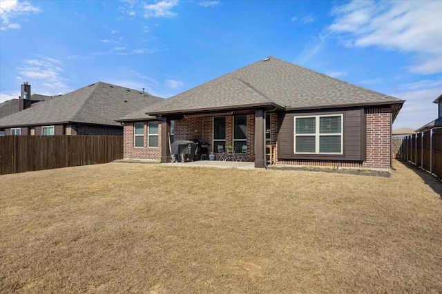 back of property featuring brick siding, a fenced backyard, a shingled roof, a patio area, and a lawn