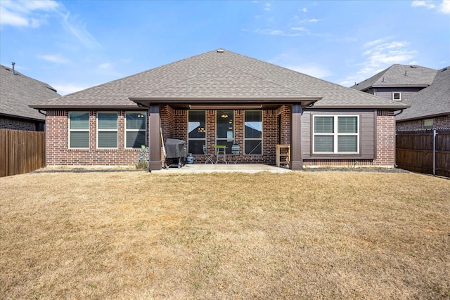 back of house with a shingled roof, a fenced backyard, brick siding, and a lawn