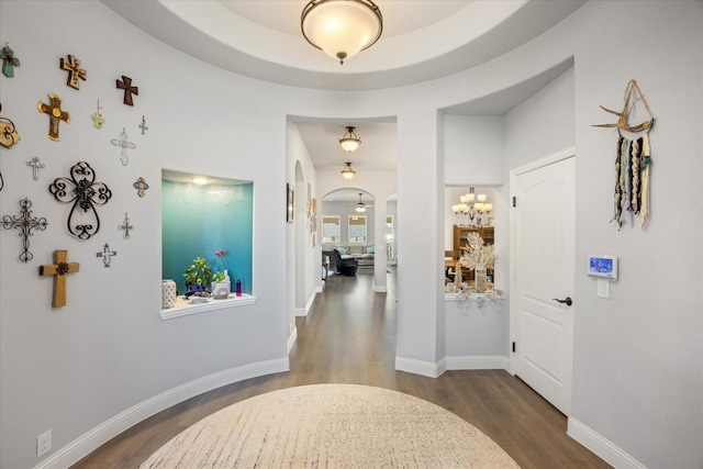 hall featuring wood finished floors, arched walkways, and baseboards