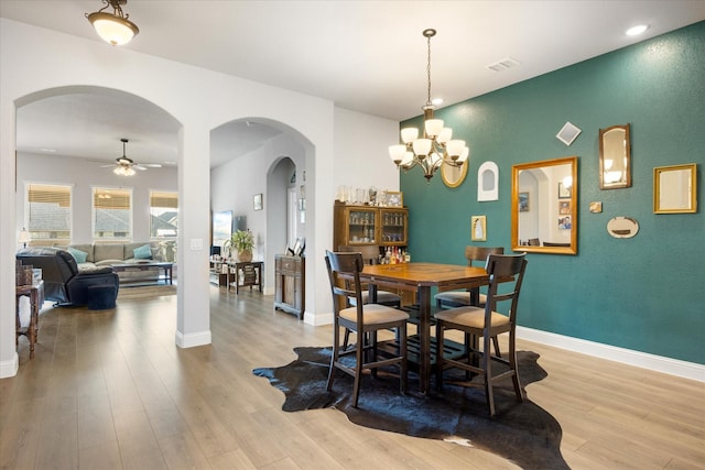 dining space featuring ceiling fan with notable chandelier, visible vents, wood finished floors, and arched walkways