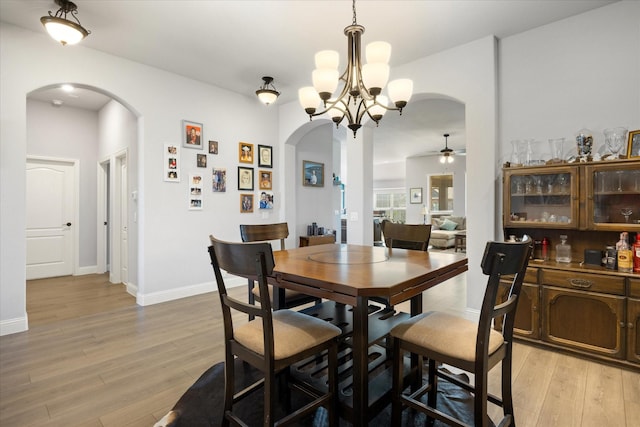 dining room featuring arched walkways, ceiling fan with notable chandelier, baseboards, and light wood-style floors