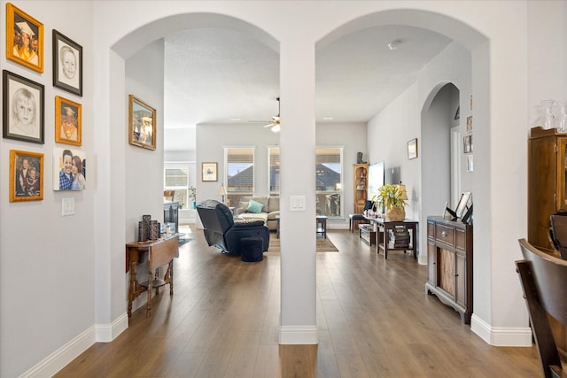 hall featuring arched walkways, baseboards, and wood finished floors