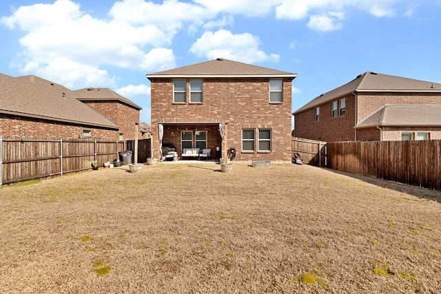 rear view of property featuring a patio, brick siding, a fenced backyard, and a lawn