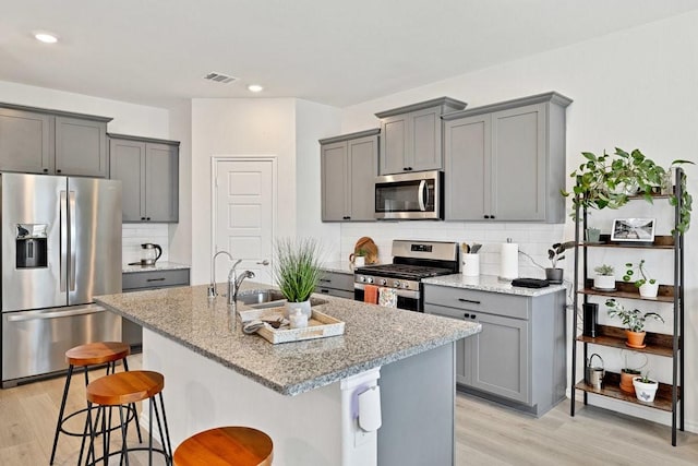 kitchen featuring light stone counters, light wood-style floors, gray cabinets, and appliances with stainless steel finishes