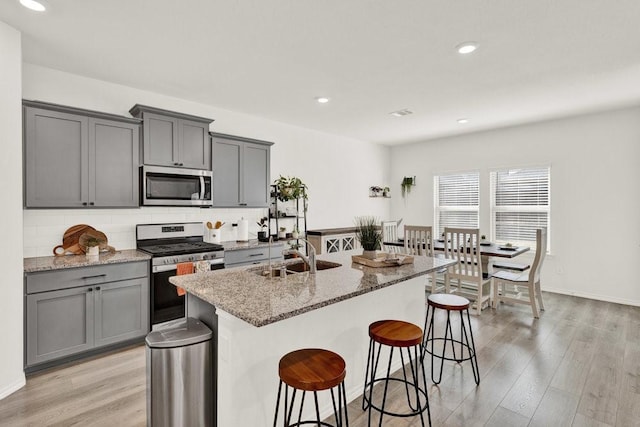 kitchen featuring light stone countertops, gray cabinets, appliances with stainless steel finishes, light wood-style flooring, and a sink