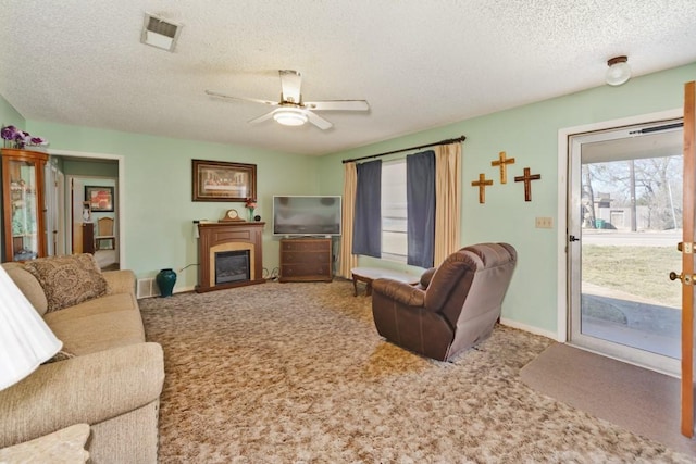 living area with carpet, visible vents, ceiling fan, a textured ceiling, and a glass covered fireplace