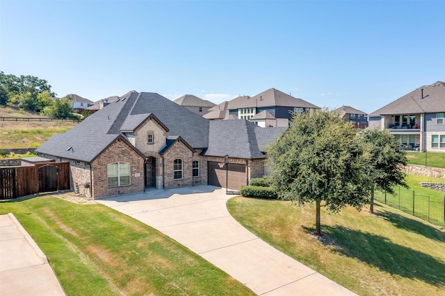 french provincial home with a front lawn, driveway, fence, a garage, and brick siding