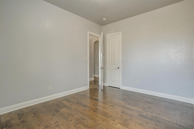 unfurnished room featuring dark wood-style floors, arched walkways, and baseboards