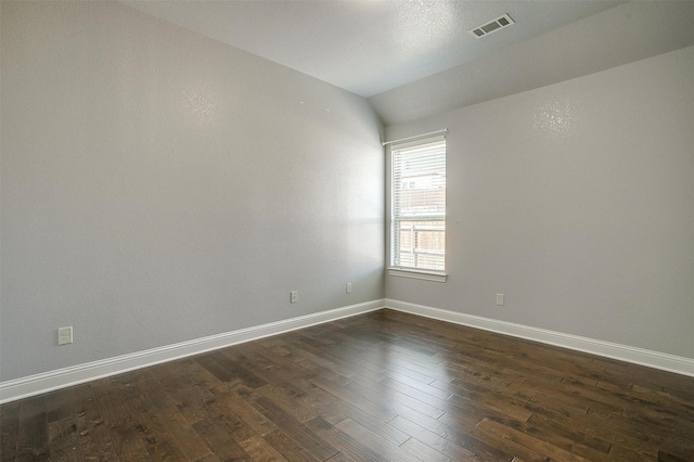 empty room featuring vaulted ceiling, dark wood-style floors, visible vents, and baseboards