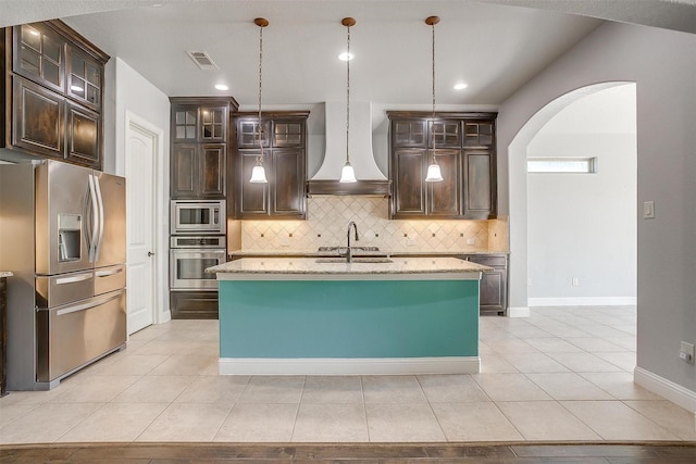 kitchen with light stone counters, stainless steel appliances, arched walkways, dark brown cabinetry, and custom exhaust hood