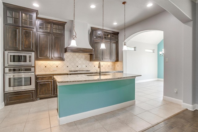 kitchen with tasteful backsplash, light stone countertops, arched walkways, stainless steel appliances, and a sink