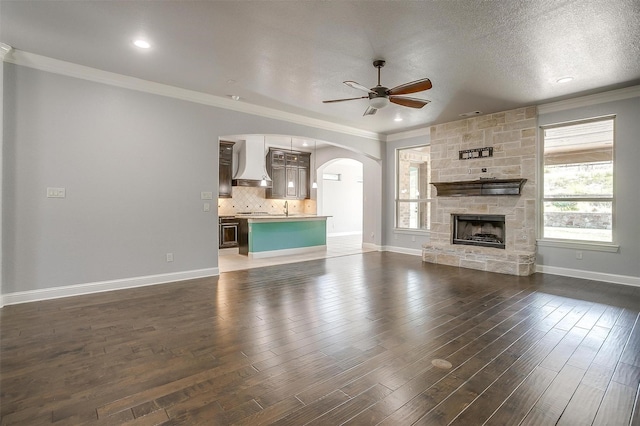 unfurnished living room featuring dark wood-style floors, arched walkways, ceiling fan, and ornamental molding