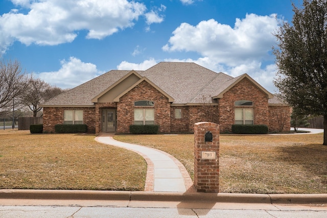 view of front facade featuring brick siding, fence, a front lawn, and roof with shingles