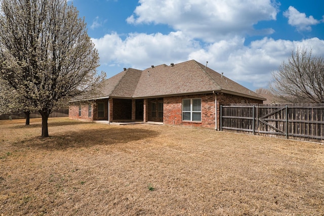 rear view of property featuring a yard, brick siding, roof with shingles, and a fenced backyard