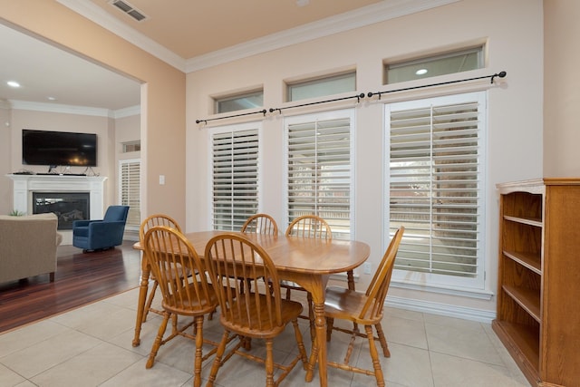 dining space with light tile patterned floors, visible vents, a glass covered fireplace, and ornamental molding