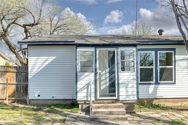 back of property featuring entry steps, fence, and roof with shingles