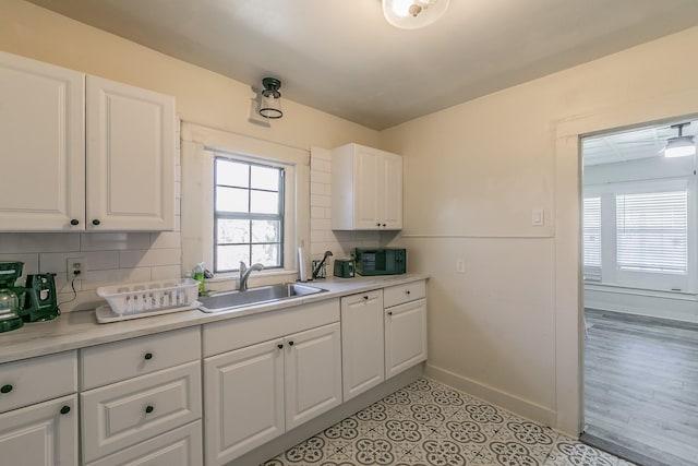 kitchen featuring a sink, baseboards, backsplash, and white cabinetry