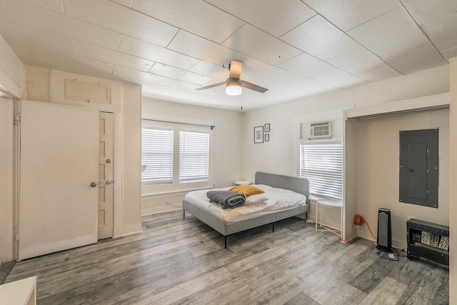 bedroom with electric panel, wood finished floors, a wall mounted AC, and ceiling fan
